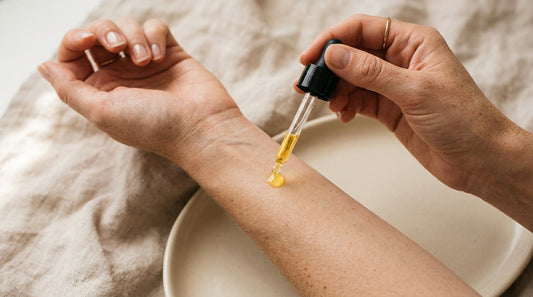 Hand applying a golden drop of natural retinol oil onto the inner forearm with a glass dropper — editorial close-up for clean, sensitive-skin-friendly anti-aging routines